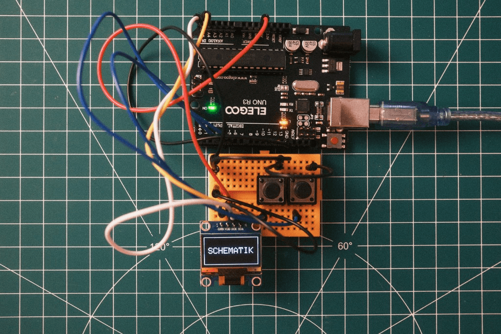 Prototype hardware on a breadboard: microcontroller, wiring, and OLED displaying SCHEMATIK